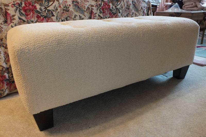 A Contemporary ottoman with button tufted seat upholstered in a soft white cotton chenille fabric