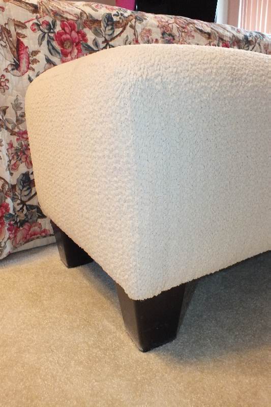 A Contemporary ottoman with button tufted seat upholstered in a soft white cotton chenille fabric