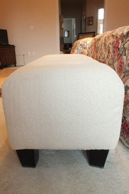 A Contemporary ottoman with button tufted seat upholstered in a soft white cotton chenille fabric