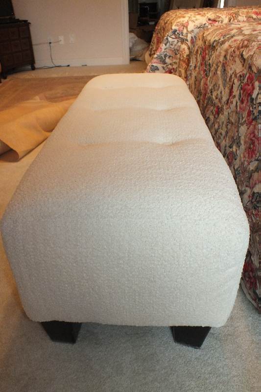 A Contemporary ottoman with button tufted seat upholstered in a soft white cotton chenille fabric