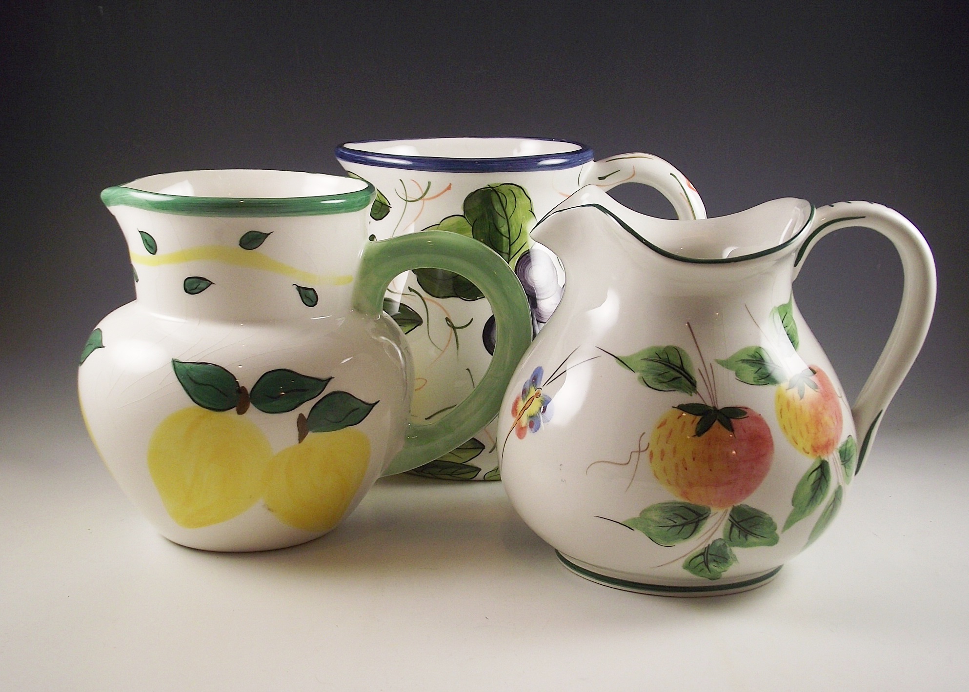 Three ceramic pitchers with painted designs.