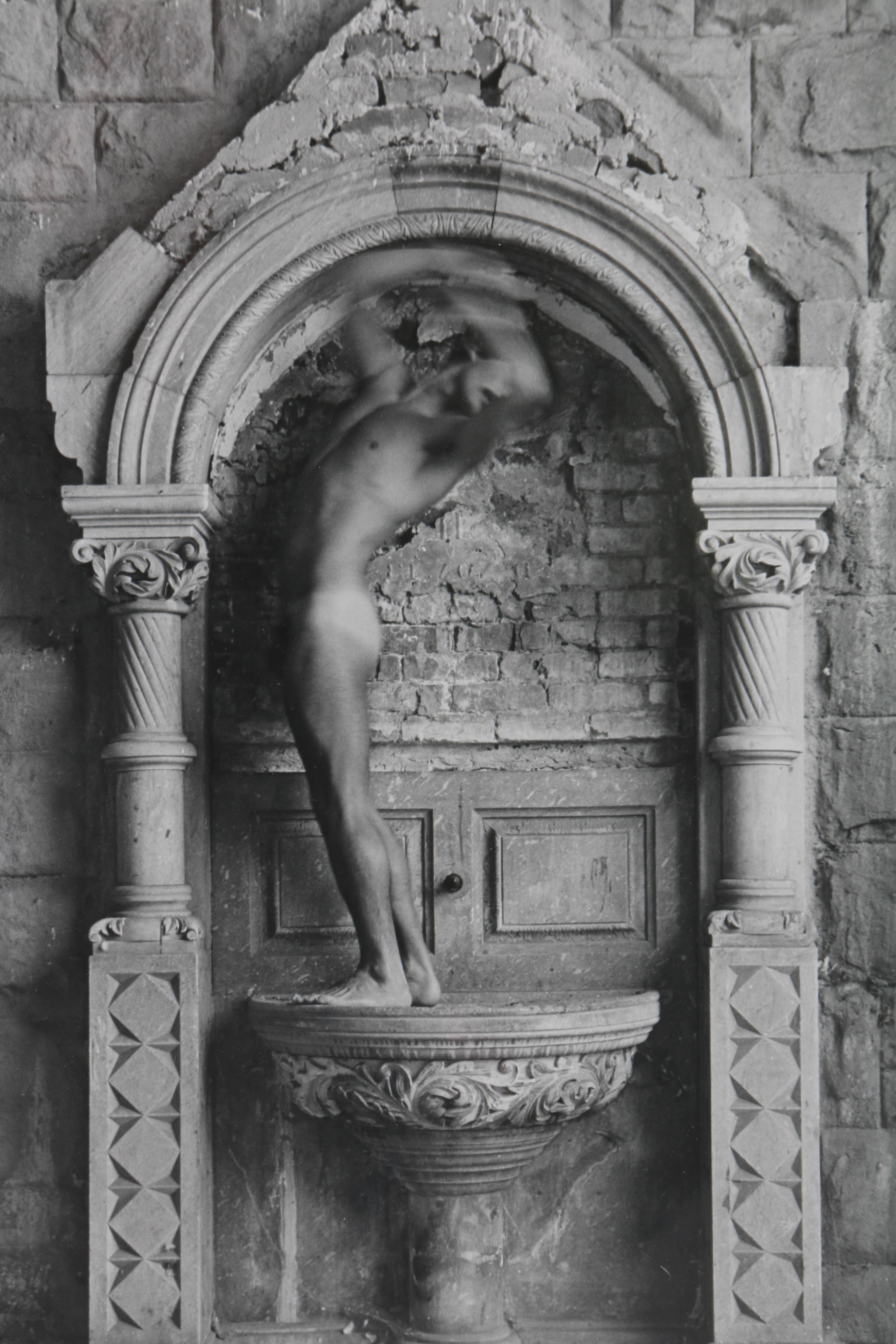 Black and White Photograph of a Nude Figure Under an Arch