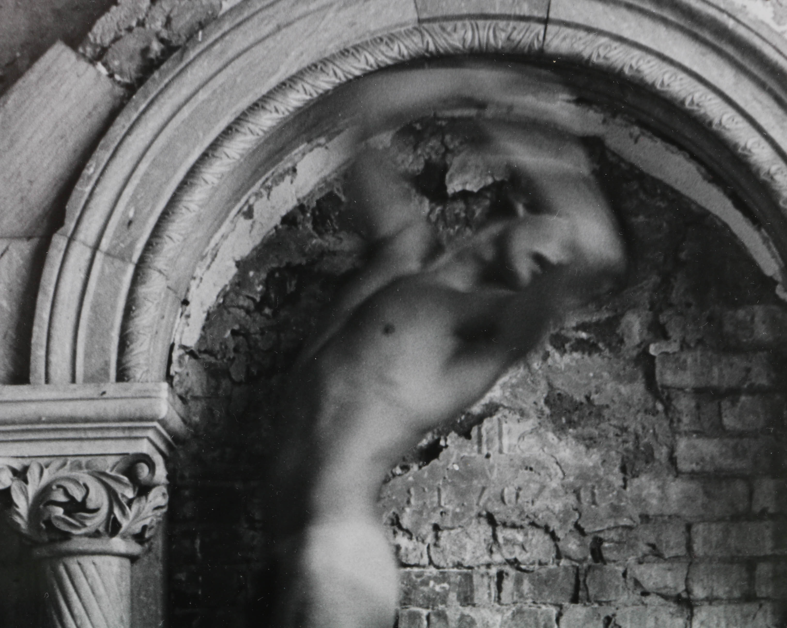 Black and White Photograph of a Nude Figure Under an Arch