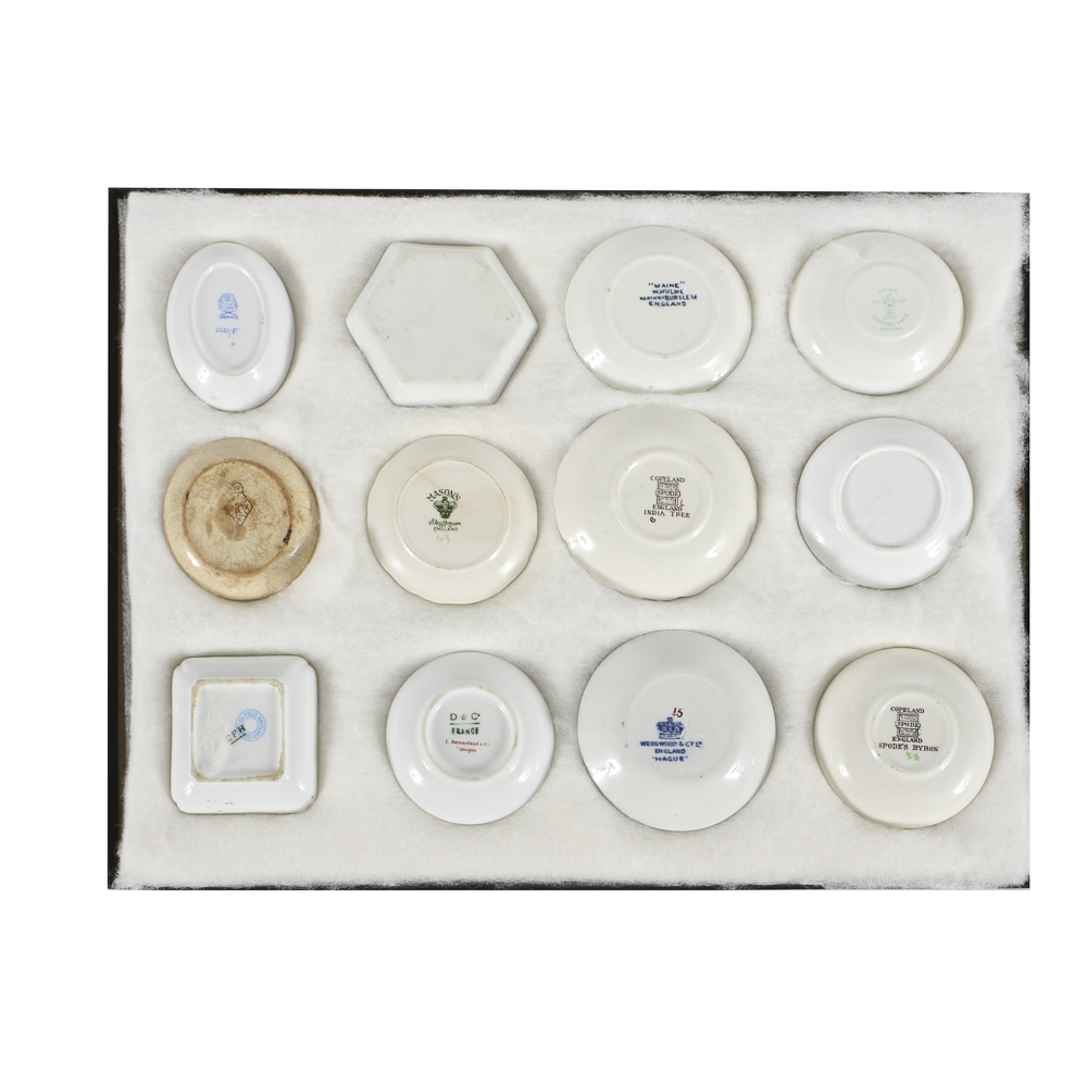 Twelve Porcelain Butter Pats In Glass Top Display Case