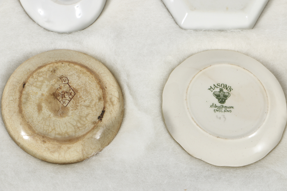 Twelve Porcelain Butter Pats In Glass Top Display Case