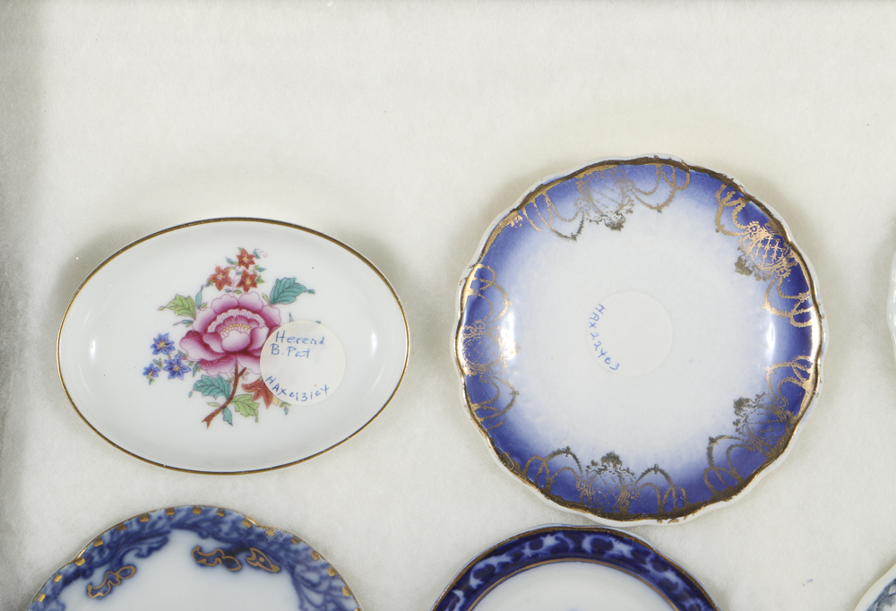 Twelve Porcelain Butter Pats In Glass Top Display Case