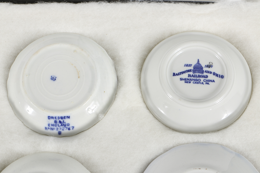 Twelve Porcelain Butter Pats In Glass Top Display Case