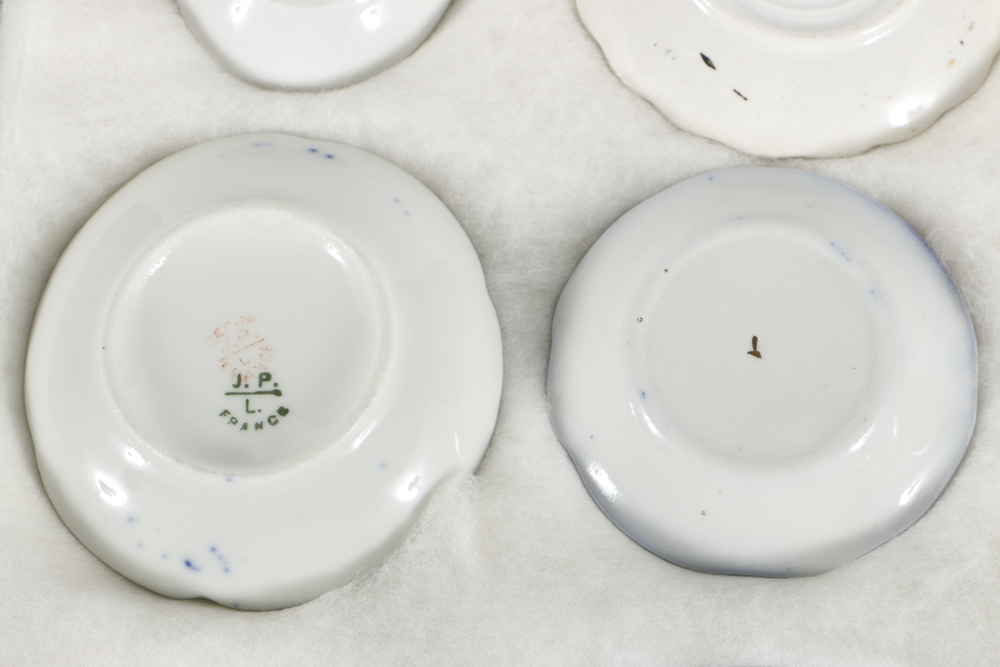 Twelve Porcelain Butter Pats In Glass Top Display Case