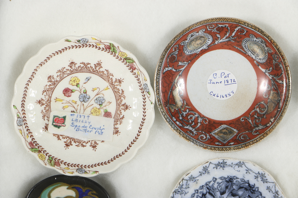 Twelve Porcelain Butter Pats In Glass Top Display Case