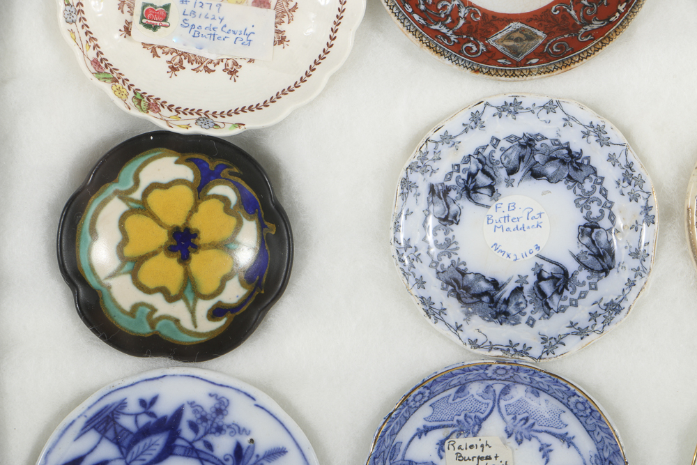 Twelve Porcelain Butter Pats In Glass Top Display Case