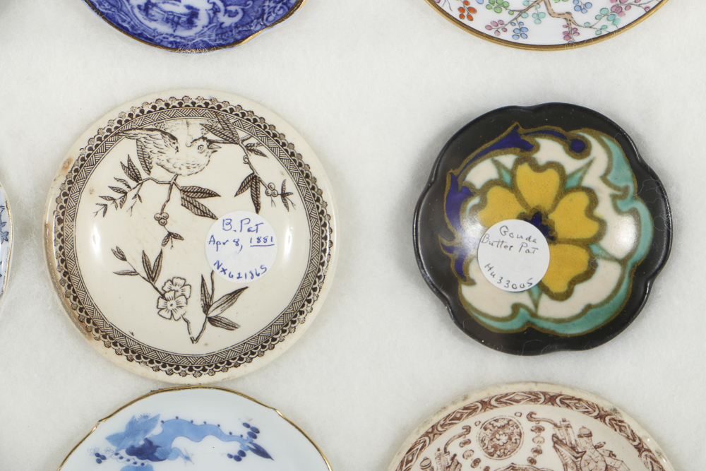 Twelve Porcelain Butter Pats In Glass Top Display Case