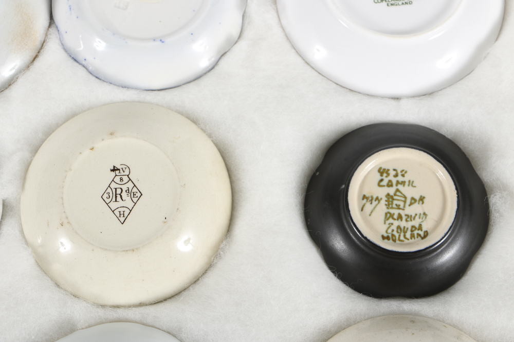 Twelve Porcelain Butter Pats In Glass Top Display Case