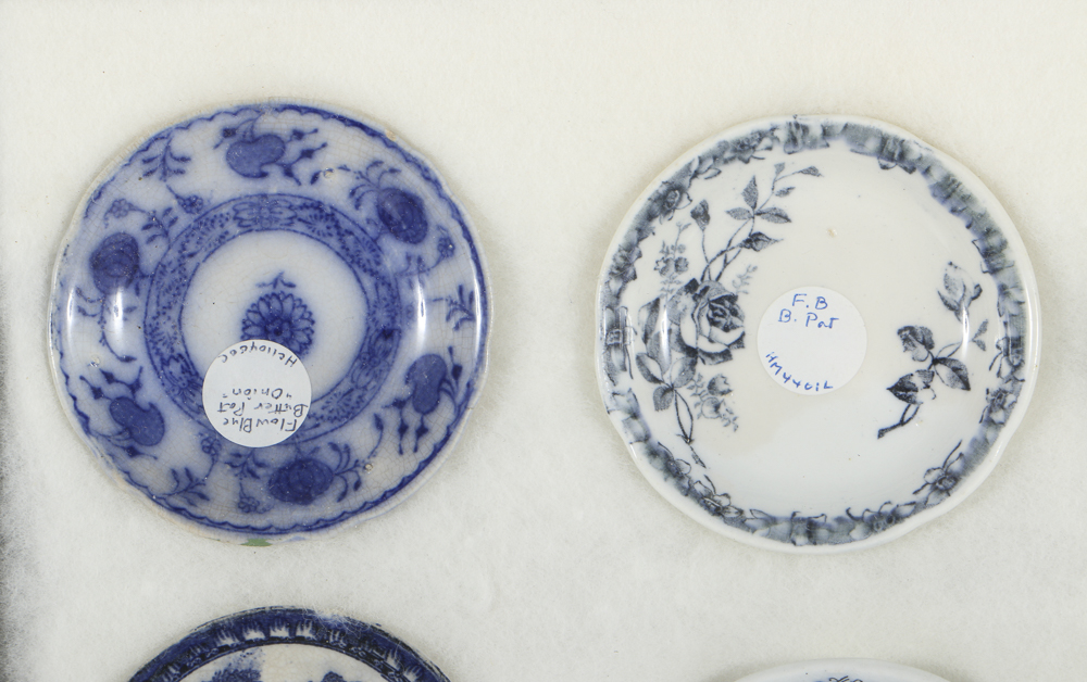 Twelve Porcelain Butter Pats In Glass Top Display Case