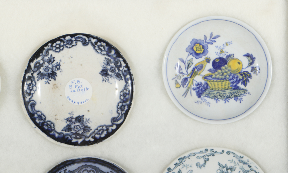 Twelve Porcelain Butter Pats In Glass Top Display Case