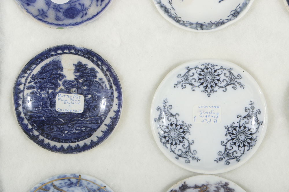 Twelve Porcelain Butter Pats In Glass Top Display Case