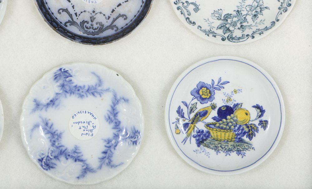 Twelve Porcelain Butter Pats In Glass Top Display Case