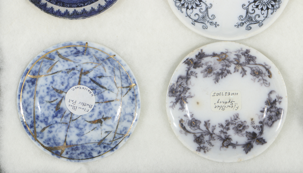 Twelve Porcelain Butter Pats In Glass Top Display Case