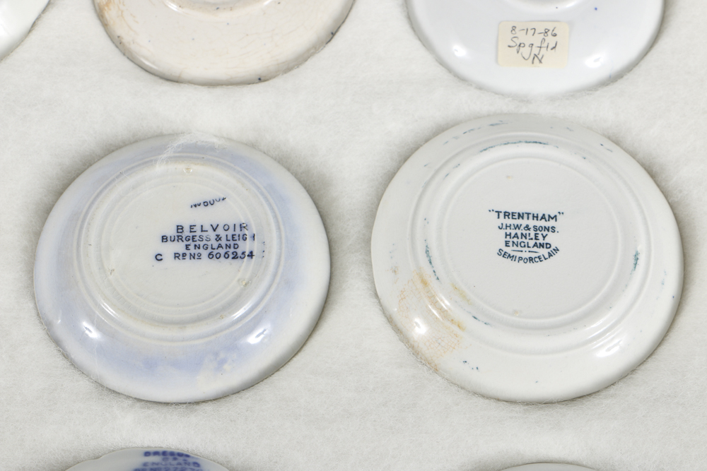 Twelve Porcelain Butter Pats In Glass Top Display Case