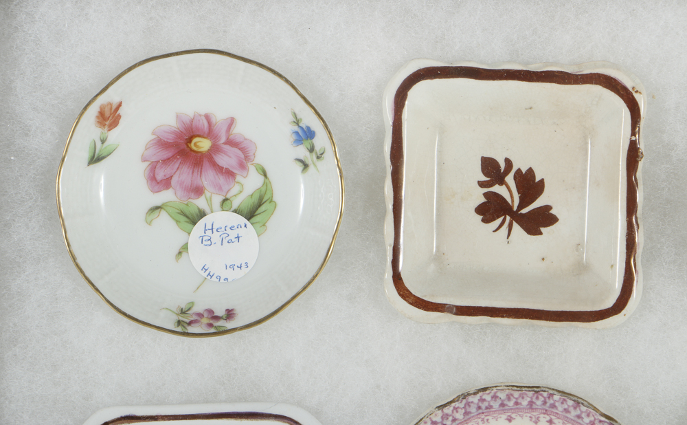Twelve Porcelain Butter Pats In Glass Top Display Case