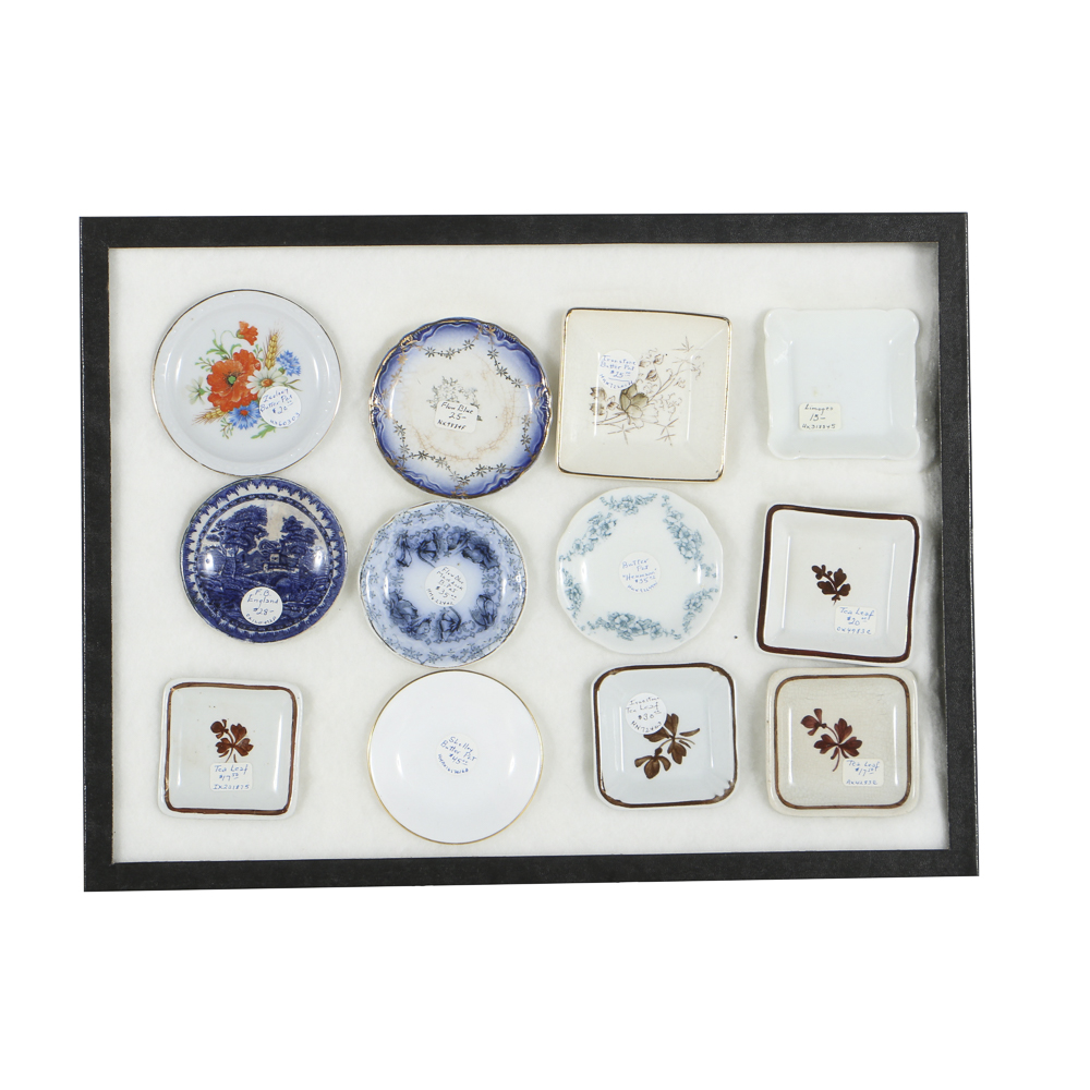 Twelve Porcelain Butter Pats In Glass Top Display Case