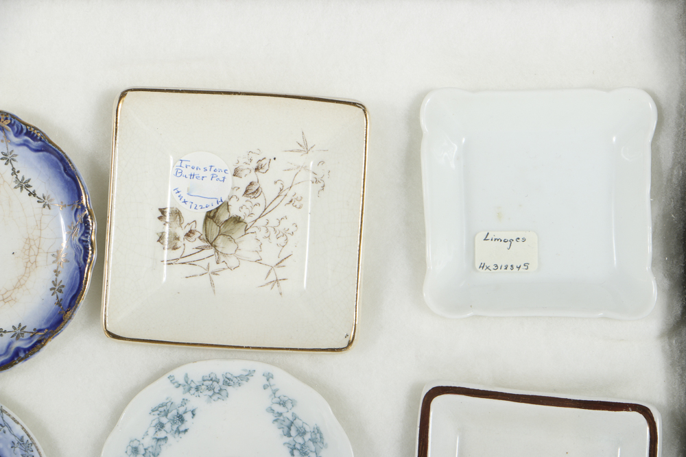 Twelve Porcelain Butter Pats In Glass Top Display Case