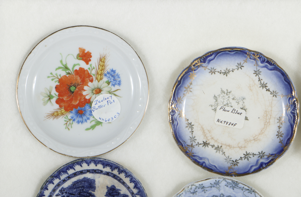 Twelve Porcelain Butter Pats In Glass Top Display Case