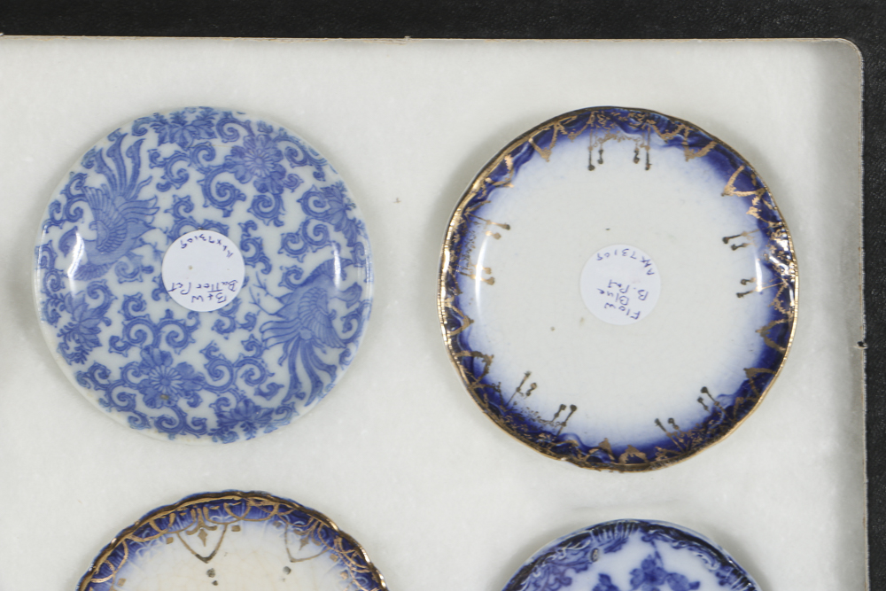 Twelve Porcelain Butter Pats In Glass Top Display Case