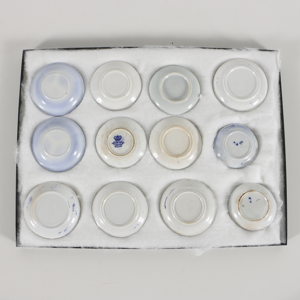 Twelve Porcelain Butter Pats In Glass Top Display Case